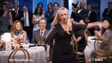 a woman in a black dress is dancing in front of a crowd with a nbc logo on the bottom