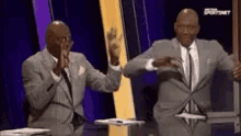 two men in suits are dancing in front of a purple wall .