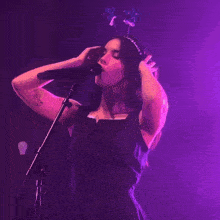 a woman with a tattoo on her arm is singing into a microphone in a dark room