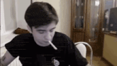 a man is smoking a cigarette while sitting at a table in a room .