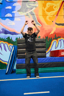 a man wearing a black shirt with a drawing of a hand on it is standing on a blue mat