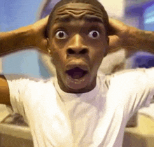 a man in a white shirt is making a surprised face while holding his head .