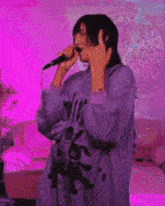 a person is singing into a microphone while wearing a purple shirt .