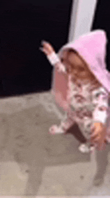a little girl wearing a pink hoodie is walking on the sidewalk .