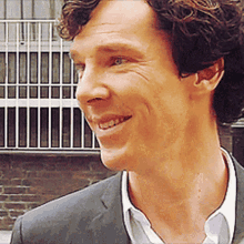 a man with curly hair wearing a suit and white shirt is smiling