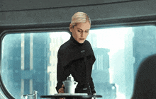 a woman in a black suit is standing in front of a window holding a silver container .