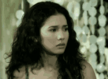 a woman with long curly hair is looking at the camera with a serious look on her face