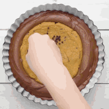 a person spreading chocolate frosting on a cookie dough in a pan