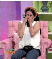 a woman is sitting in a pink chair with her hands on her face .