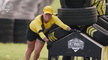 a woman in a yellow shirt is pushing a stack of tires with a sign that says ultimate challenge