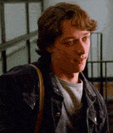 a young man wearing a denim jacket and a striped shirt looks at the camera