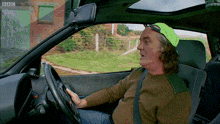 a man wearing a green hat is driving a car with bbc written on the side