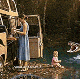a woman in a blue dress stands next to a snake and a baby sitting on the shore