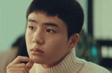 a young man wearing a white turtleneck sweater looks at something