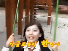 a girl in a school uniform is sitting on a swing in a playground with korean writing behind her