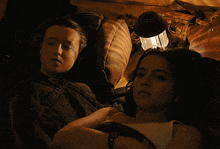 two girls are laying in a dark room with a lantern on the floor