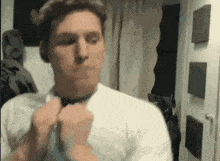 a man in a white shirt adjusts his tie in front of a mirror