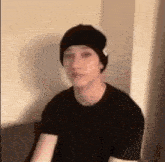 a man wearing a black beanie and a black shirt is sitting on a couch .