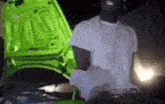 a man is standing next to a green car with the hood open .