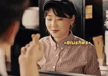 a woman wearing a plaid shirt and a hat is making a heart shape with her hand .