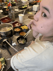 a woman sits at a table with bowls of food and chopsticks in front of her