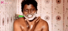 a shirtless man is shaving his face in a bathroom with foam on his face .