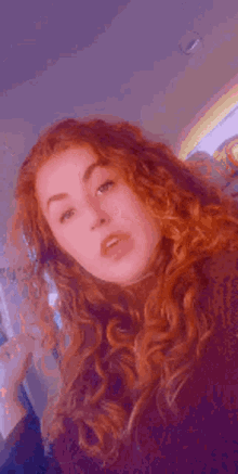 a young woman with red curly hair is taking a selfie with her phone .