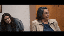 two women are sitting next to each other in a room and smiling