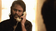 a man with glasses is talking on a yellow telephone