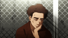 a man leans against a chain link fence with his head resting on his hand