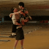 a man is carrying a woman in his arms in a bowling alley