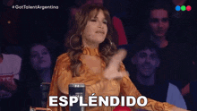 a woman is giving a thumbs up in front of a crowd and the word esplendido is on the screen behind her