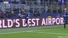 a soccer player celebrates a goal in front of a sign that says " world 's best airport "