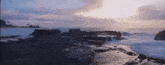 a sunset over the ocean with rocks in the foreground