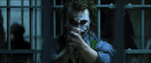 the joker is holding a gun in a jail cell and pointing it at the camera .