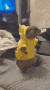 a squirrel wearing a yellow hoodie stands on a bed