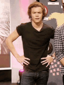 a man in a black shirt stands with his hands on his hips in front of a sign that says ' harry ' on it