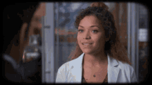 a woman with curly hair is smiling and wearing a lab coat
