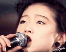 a woman singing into a microphone with syron written on the bottom right