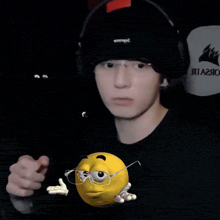 a man wearing a black hat and headphones holds a yellow smiley face