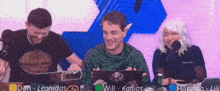 a group of people are sitting at a table with their laptops and one of them has the name will on his laptop