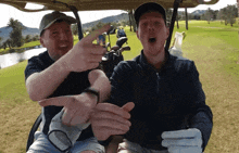 two men are sitting in a golf cart and one of them is pointing