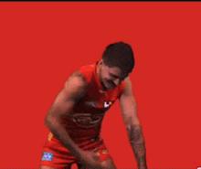 a man with a mustache is wearing a red tank top and shorts and is dancing on a red background .