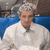 a young man with curly blonde hair is sitting in a blue chair in a restaurant .
