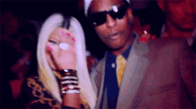 a man in a suit and tie stands next to a woman in sunglasses