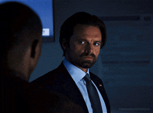 a man in a suit and tie is looking at another man in a dark room with the words thenameswintergifs below him