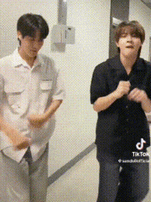 two young men are standing next to each other in a hallway and dancing .