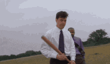a man in a tie is holding a baseball bat in a field