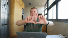 a man is making a heart shape with his hands in front of a laptop