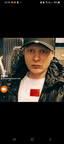 a phone screen shows a man wearing a black hat and a white shirt with the word room on it